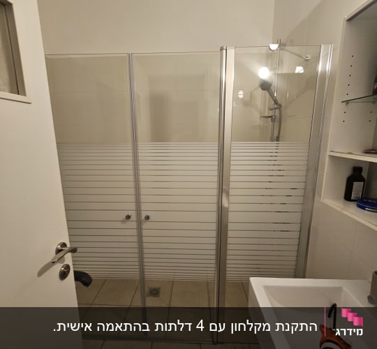 מקלחת עם דלתות זכוכית וכלי עבודה על הכיור